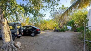 Un sendero de tierra que lleva a un coche y una motocicleta estacionados, rodeado de árboles y vegetación.