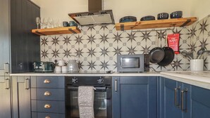 Een keuken met donkerblauwe kastjes, een magnetron, een waterkoker en een branddeken.