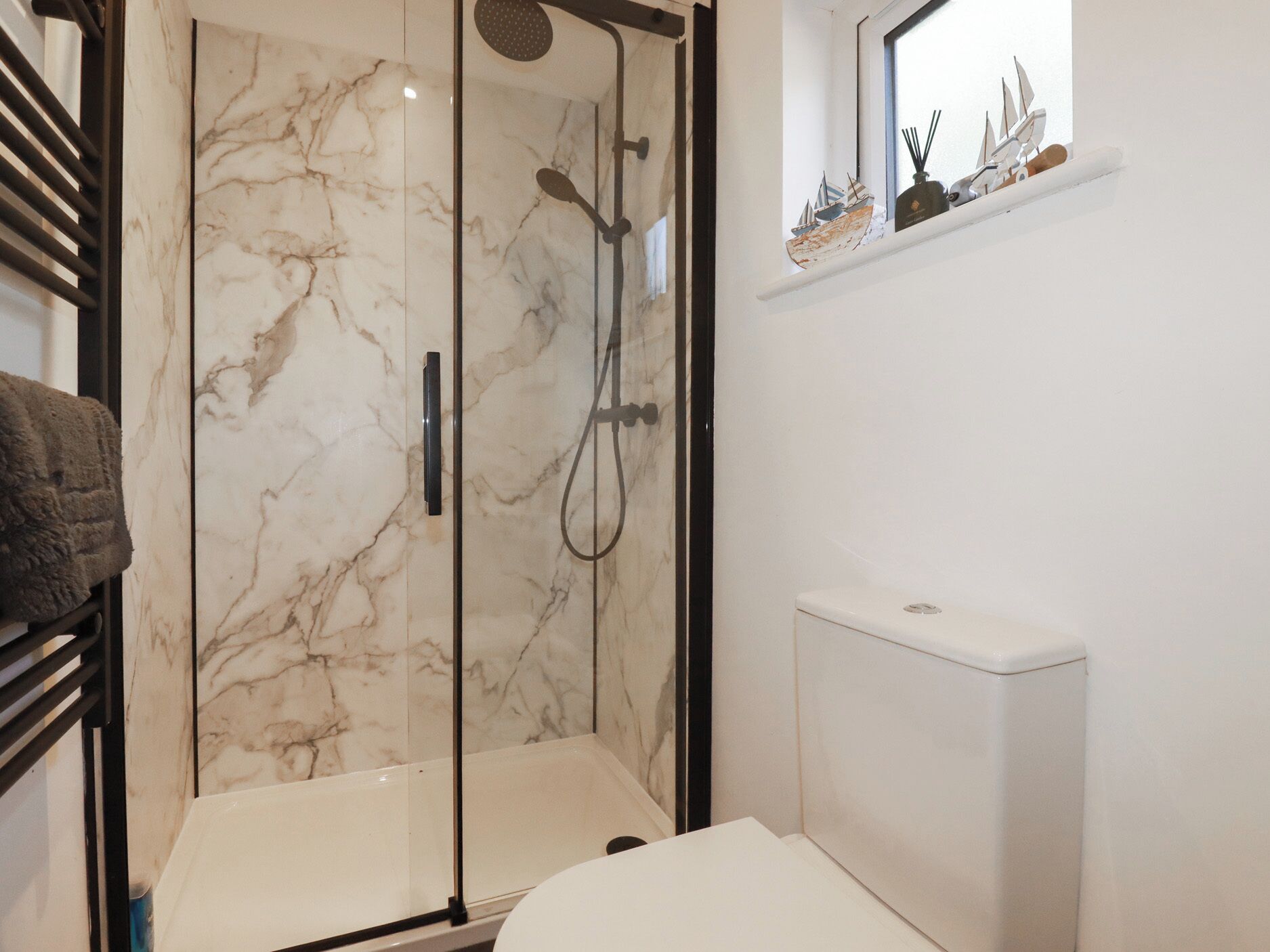 A bathroom with a glass-enclosed shower, a white toilet, and a small shelf with decorative items.