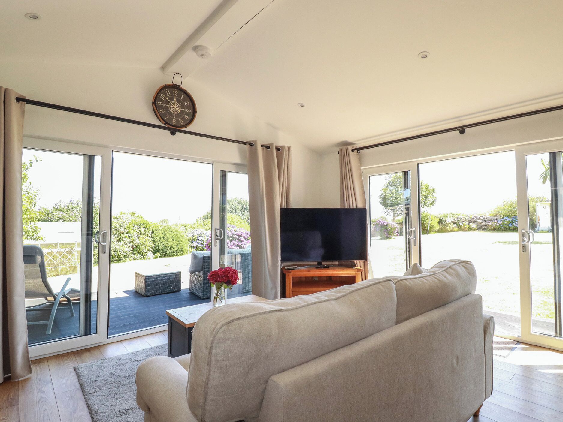 A living room with a sofa, a television, and a view of the outdoors through large glass doors.