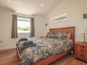 Ein Schlafzimmer mit einem hölzernen Bett, einem Nachttisch, einem Fenster mit Vorhängen und einem kleinen Tisch mit einer Lampe.