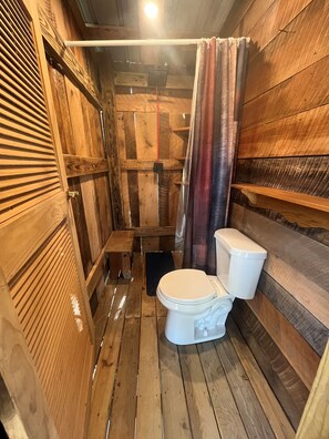 A wooden bathroom with a toilet, shower, and wooden walls. - The Bunkhouse (New Lexington)