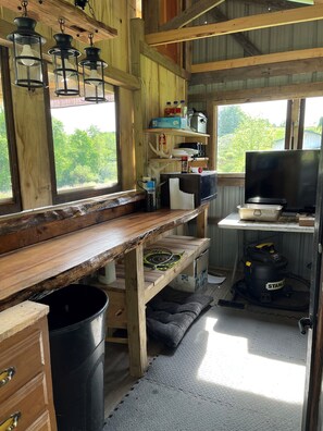 Ein rustikales Blockhaus-Interieur mit einem Holztisch, Regalen mit verschiedenen Gegenständen, einem Fernseher und einem Staubsauger.