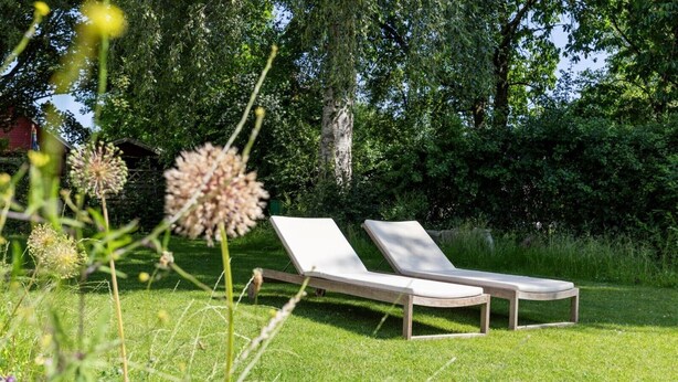 Deux fauteuils de jardin sont placés sur une pelouse verdoyante, avec des arbres en arrière-plan.