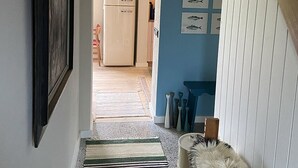 Un couloir mène à une cuisine équipée d’un réfrigérateur, où se trouve un chien, et un mur bleu orné de motifs représentant des poissons.