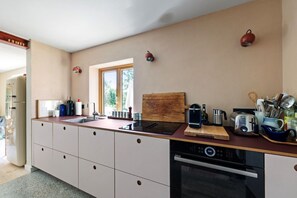 A modern kitchen with a built-in oven, a sink, and a window providing natural light. - Four Cows Vacation Home – A Rural Retreat Near the Baltic Sea (Esgrus)