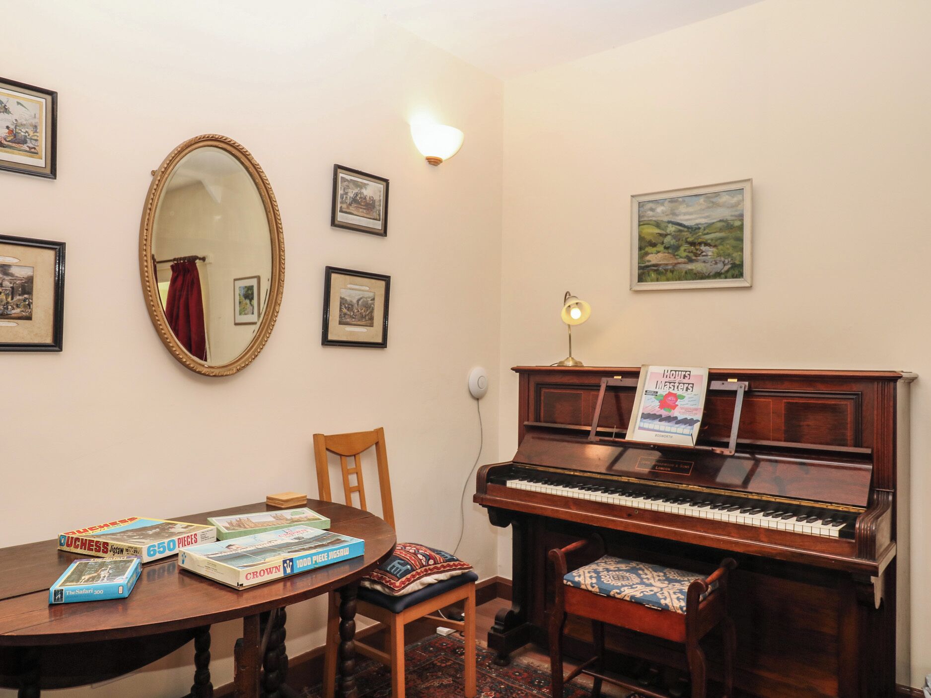 Una habitación con un piano, una mesa con rompecabezas, cuadros en la pared y un espejo.