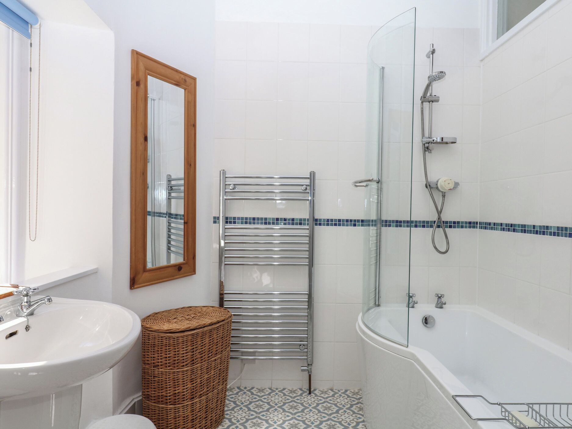 A bathroom with a glass shower enclosure, a white sink, a mirror, and a wicker basket.