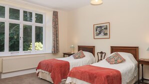 A bedroom with two single beds, a window with curtains, a radiator, a framed picture on the wall, and a hanging light fixture. - Lukesland Wing (Ivybridge)