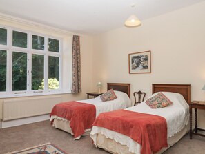 A bedroom with two single beds, a window with curtains, a radiator, a framed picture on the wall, and a hanging light fixture. - Lukesland Wing (Ivybridge)