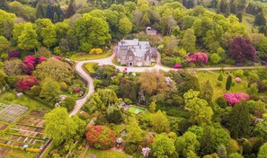 Un vaste domaine comprenant une demeure principale au centre, entourée de jardins luxuriants et accessible par une longue allée sinueuse.