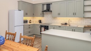 A modern kitchen with grey cabinets, a white refrigerator, a microwave, a coffee maker, and a sink. - Lukesland Wing (Ivybridge)