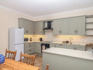 A modern kitchen with grey cabinets, a white refrigerator, a microwave, a coffee maker, and a sink. - Lukesland Wing (Ivybridge)