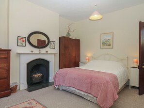 A bedroom with a bed, a fireplace, a wooden wardrobe, a nightstand, and a wall-mounted lamp. - Lukesland Wing (Ivybridge)