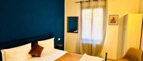 Ein Hotelzimmer mit Bett, Sessel, Schreibtisch und einem fenster mit Vorhängen.