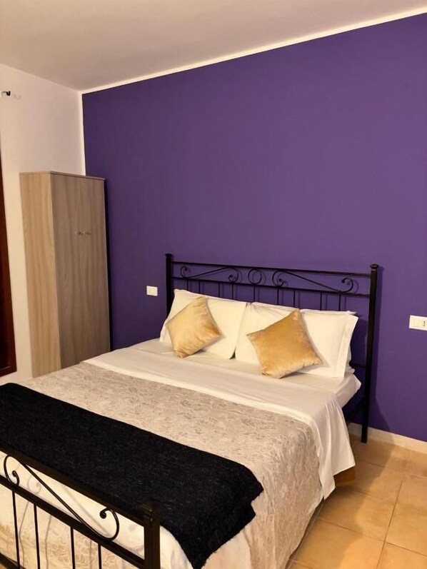 Una cama individual con estructura metálica, una colcha blanca y dos almohadas.