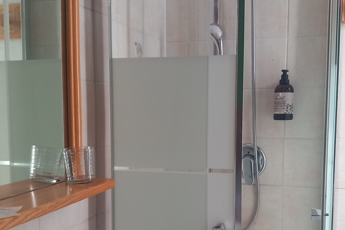 Un bagno con box doccia in vetro, un lavandino con specchio sopra e un cartello con su scritto 'ALLARME'.