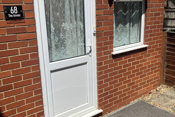 A brick house with a white door and window, a number plate reading '68 The Annex', and a small window above the door.