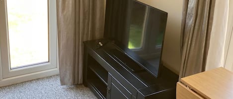 A black entertainment unit with a television, a wooden cabinet, and a window with curtains.