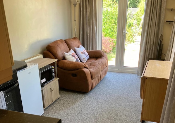 A compact living space with a sofa, a small kitchenette, and a sliding glass door to a garden. - Yeovil 1-bed Annex Sleeps 2 With Wifi (Yeovil)