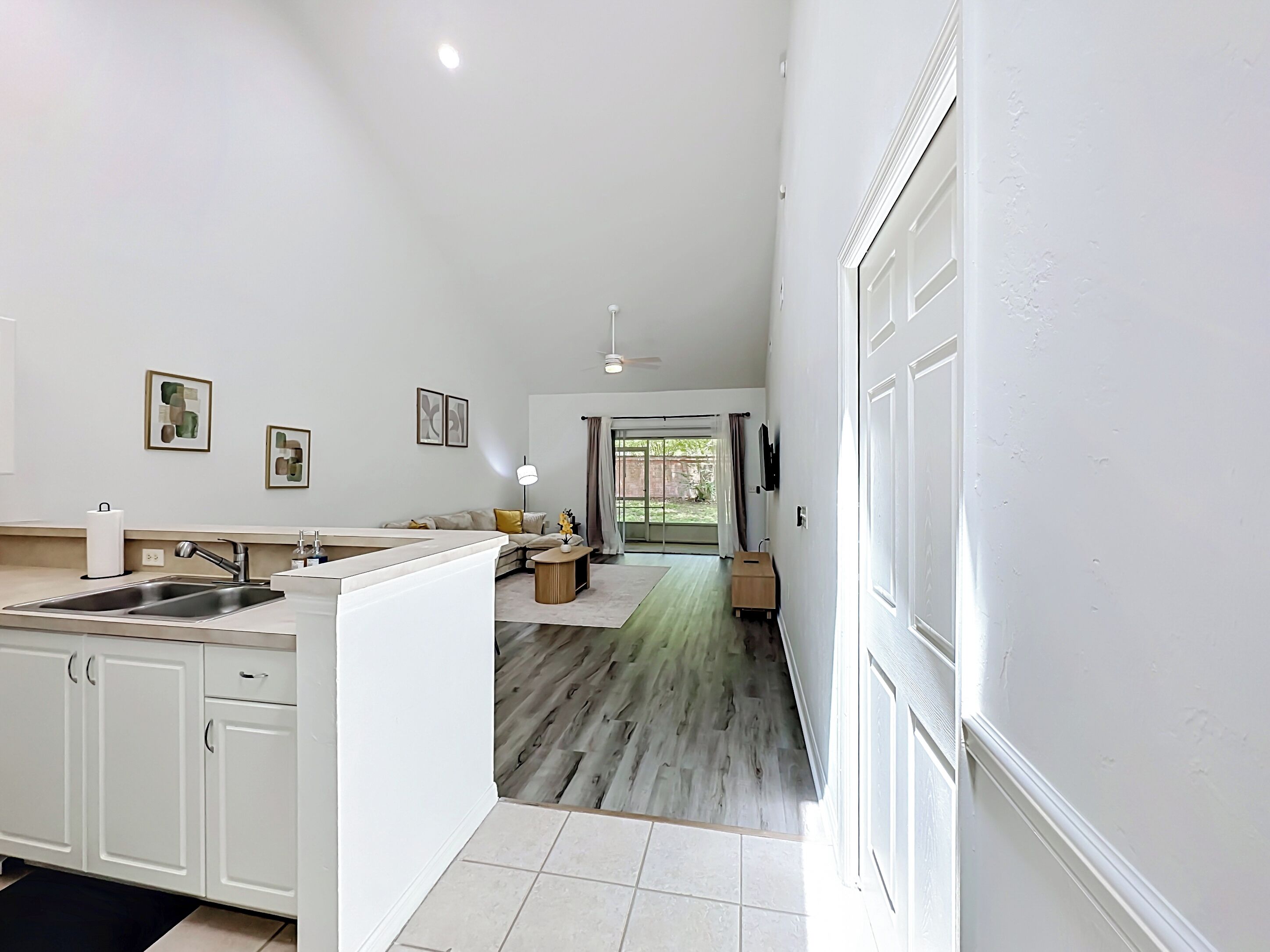 Una cocina moderna con armarios blancos, un fregadero y una zona de comedor con un sofá y una mesa.