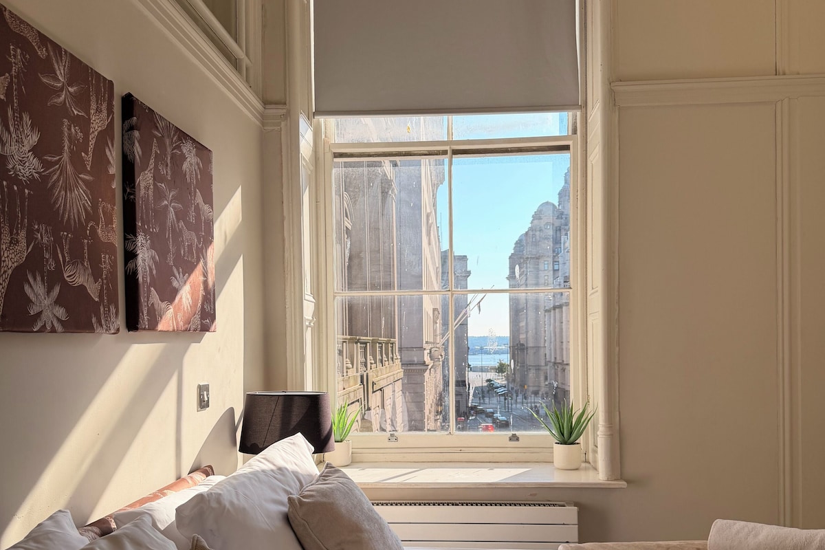 Una camera da letto con un'ampia finestra, un letto, un comodino e due quadri appesi al muro.