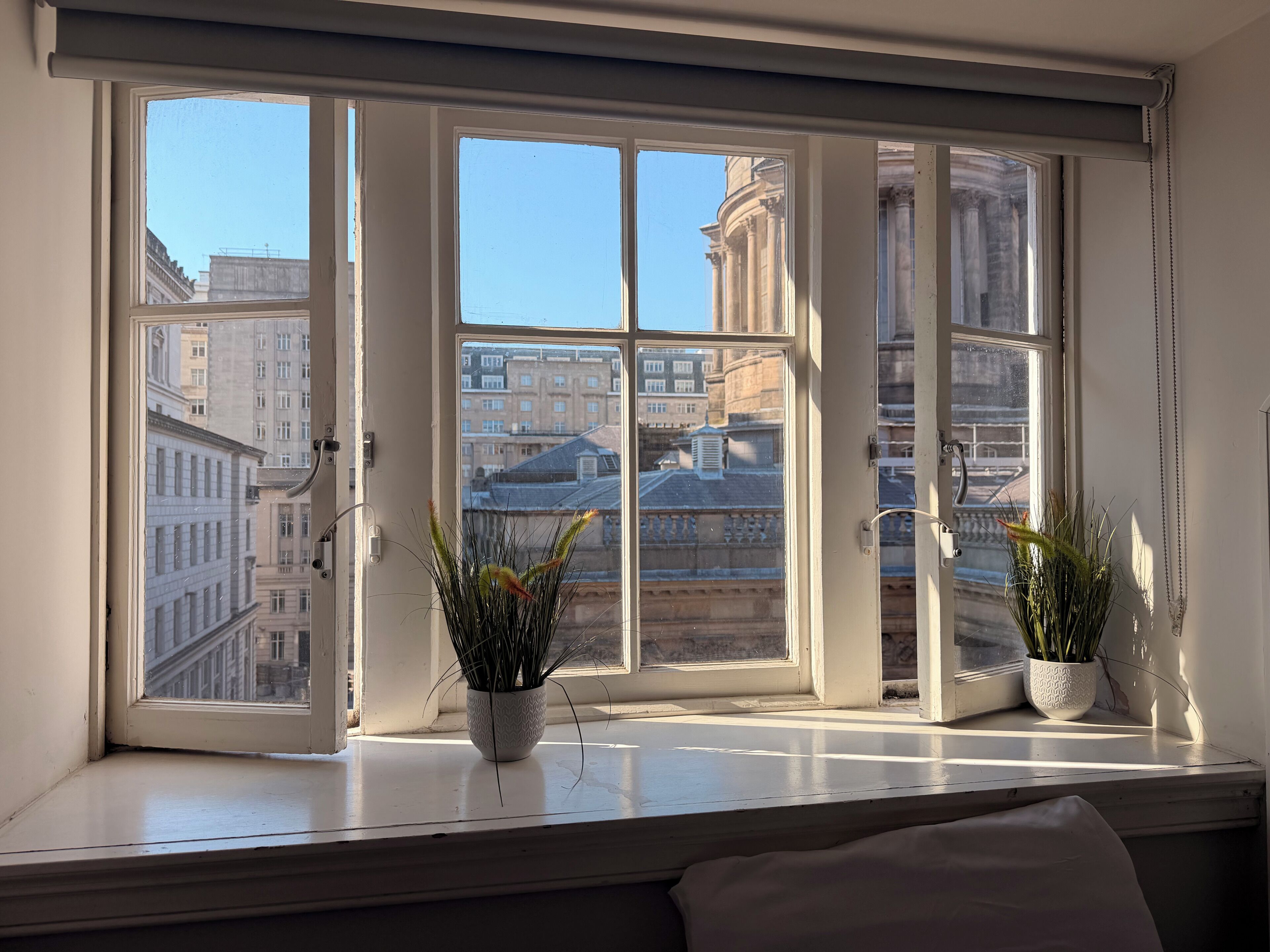 A window with a view of buildings and two potted plants on the sill.