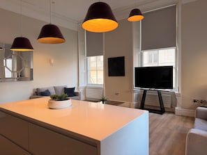 A modern kitchen with pendant lights, a large island, a flat-screen TV, and a window with a view. - Swiss Apartments (Liverpool)
