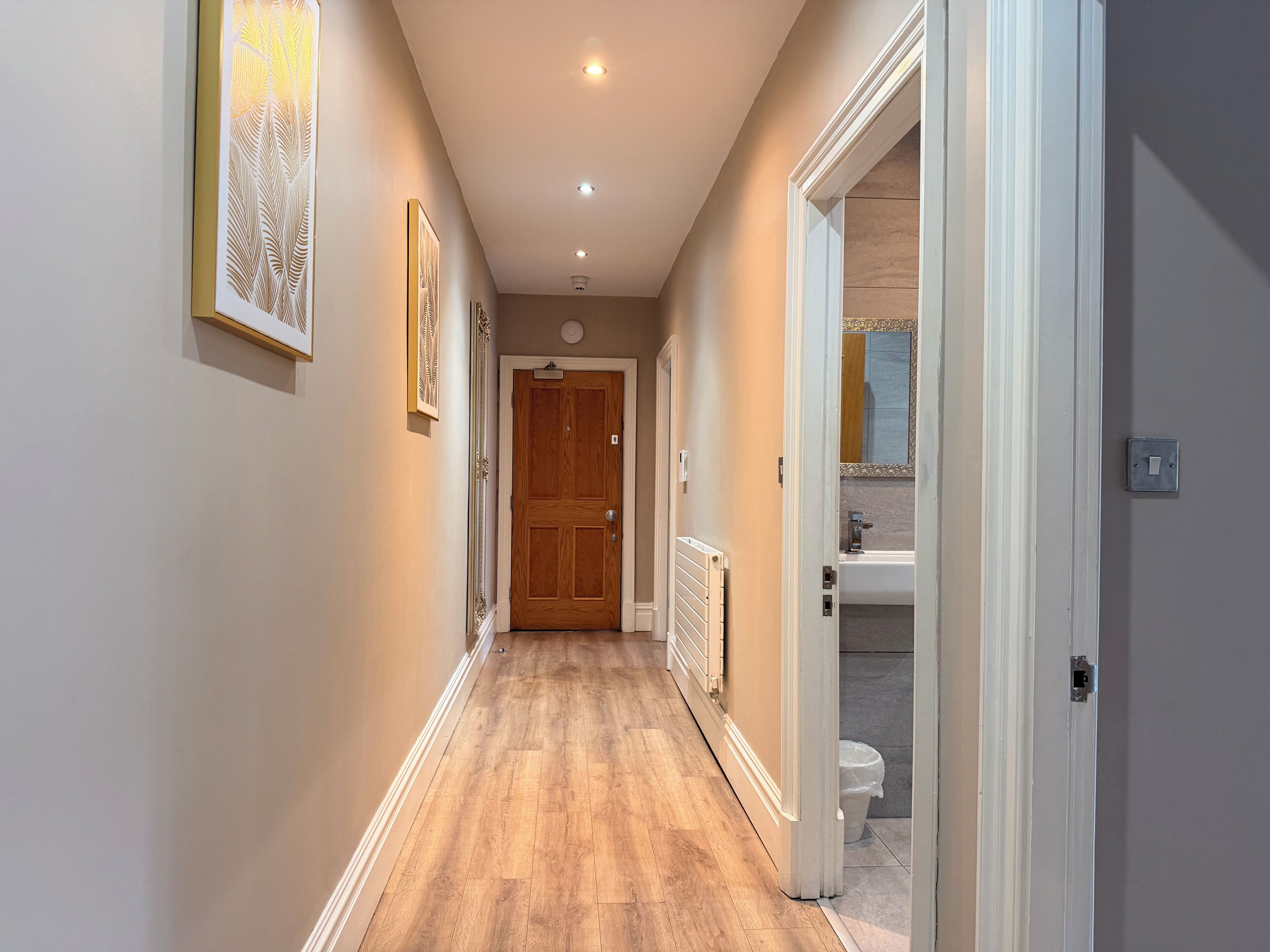 Un couloir doté d’un plancher en bois, d’un radiateur et d’une porte donnant sur une salle de bain.