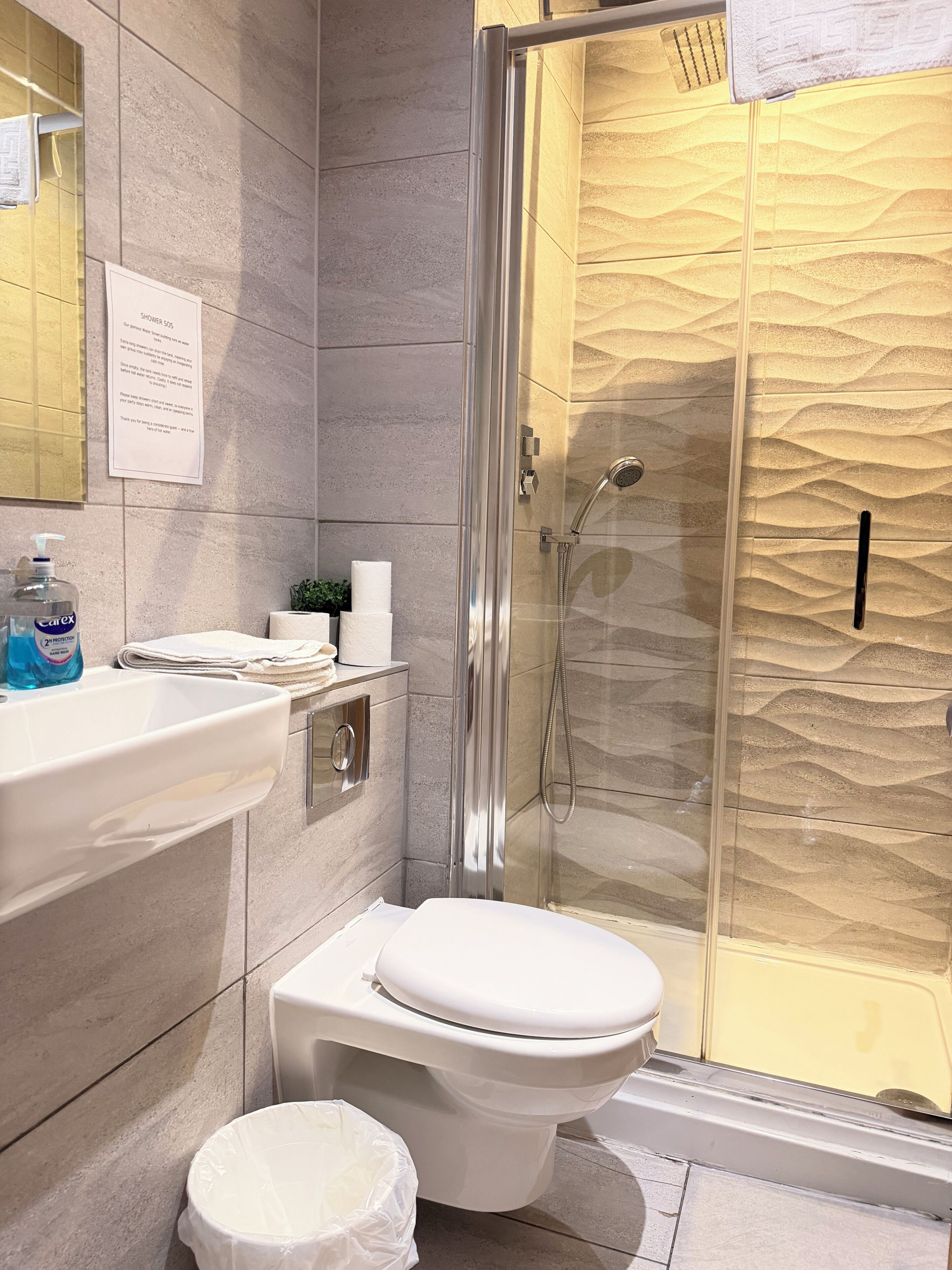 A modern bathroom with a glass-enclosed shower, a white toilet, and a sink with a soap dispenser.