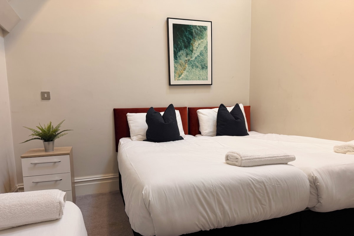 Una camera d'albergo con un letto, un comodino con una pianta, un quadro appeso alla parete e un letto rifatto con asciugamani.