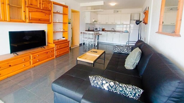 A living room with a black sofa, wooden cabinets, a television, and a kitchen in the background. - Amadores Paradise – Entire House (2 Connected Apartments) with the Complex's Pool (Mogán)