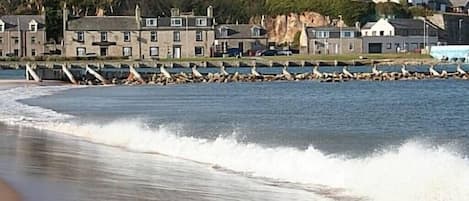 Un pueblo costero con edificios de piedra, un litoral rocoso y olas rompiendo sobre la playa.