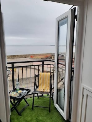 Un balcón con una silla y una mesa, con vista a una playa y un cielo despejado.