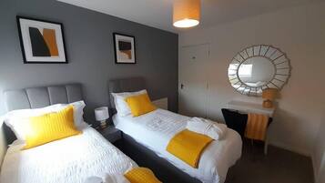 Habitación de hotel con dos camas, un escritorio, una silla, una lámpara y un espejo.