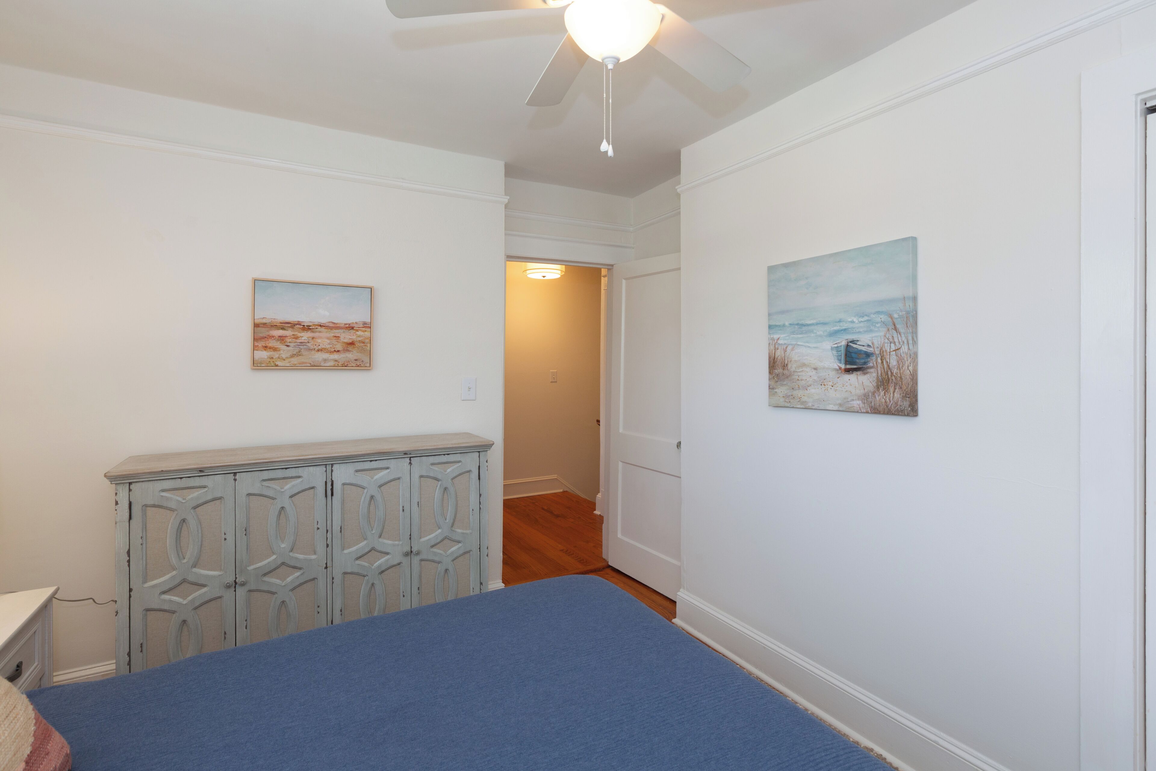A bedroom with a bed, a dresser, and two paintings on the walls.