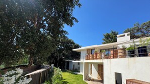 A modern house with a spacious backyard, a wooden deck, and a large tree providing shade. - Architect-designed villa with a pool and a view of the Mediterranean – Sleeps 9 (Rayol-Canadel-sur-Mer)