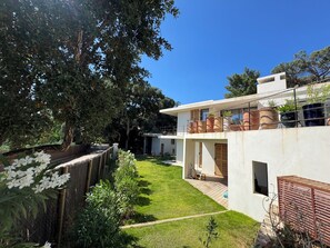 A modern house with a spacious backyard, a wooden deck, and a large tree providing shade. - Architect-designed villa with a pool and a view of the Mediterranean – Sleeps 9 (Rayol-Canadel-sur-Mer)