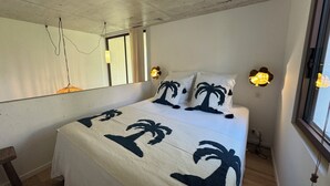 A bedroom with a bed, a bedside table, a mirror, and a window with curtains. - Architect-designed villa with a pool and a view of the Mediterranean – Sleeps 9 (Rayol-Canadel-sur-Mer)