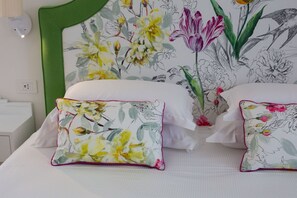 Quarto com cabeceira verde, papel de parede floral e duas camas brancas com almofadas a combinar.