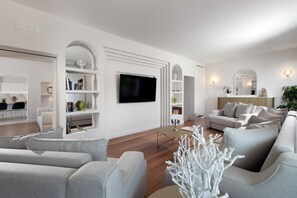 A modern living room with a flat-screen TV, grey sofas, and a white decorative tree. - Luxury Authentic Italian Villa with Private Pool & Iconic Seaview Terrace (Massa Lubrense)