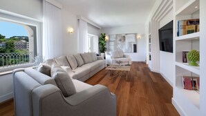 A modern living room with a sofa, armchairs, and a coffee table. There is a bookshelf with books and decorative items. - Luxury Authentic Italian Villa with Private Pool & Iconic Seaview Terrace (Massa Lubrense)