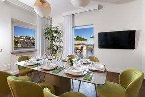 A dining area with a table set for six, chairs, a plant, and a TV on the wall. - Luxury Authentic Italian Villa with Private Pool & Iconic Seaview Terrace (Massa Lubrense)