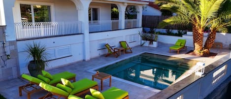 Zona junto a la piscina con sillones de descanso y una palmera.