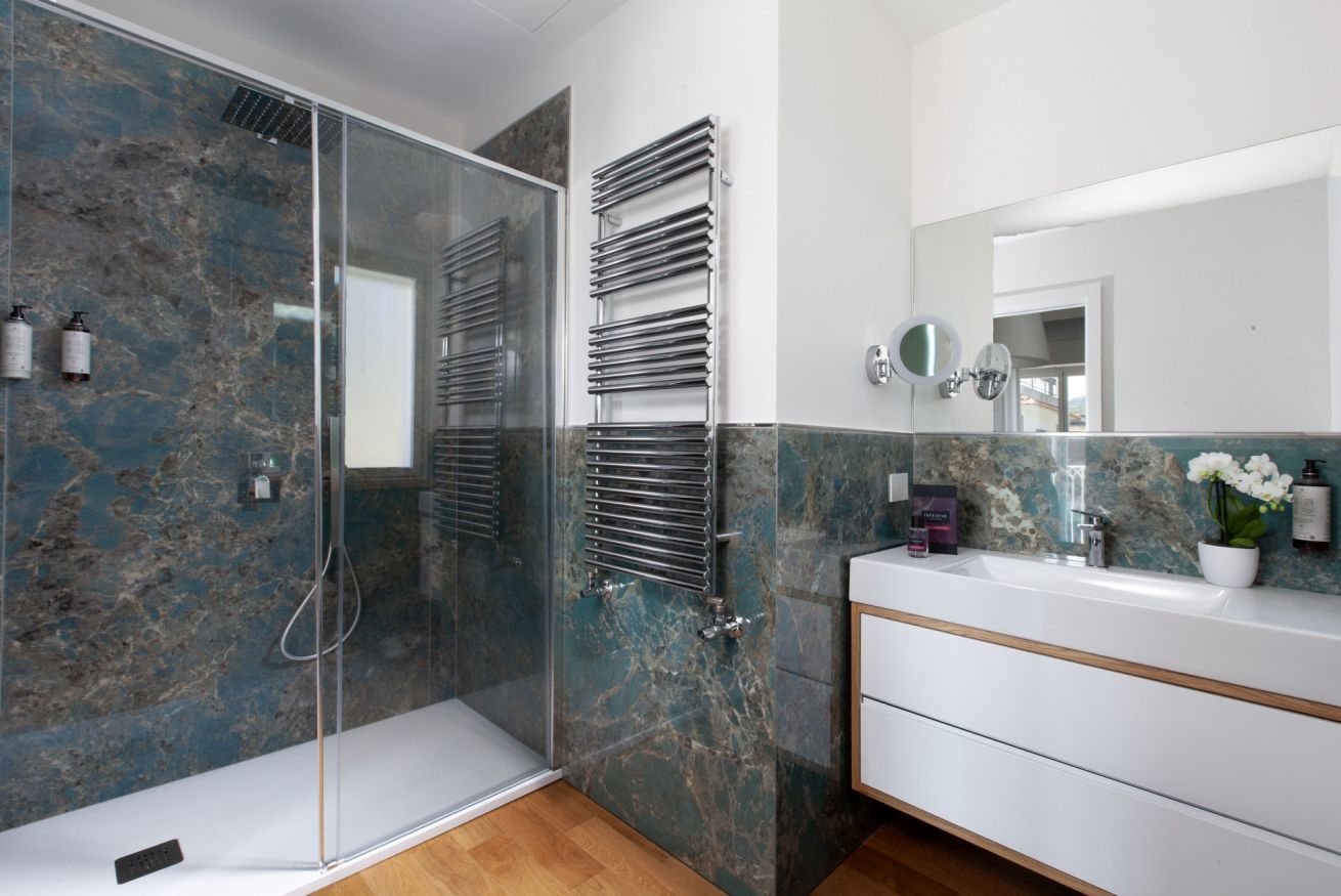 A modern bathroom with a glass shower enclosure, a white vanity with a mirror, and a marble-tiled wall.