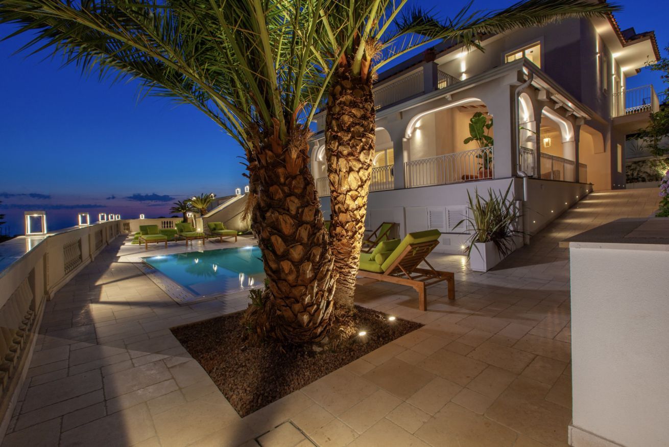 Una villa moderna con piscina, area salotto esterna e un balcone con vista sul mare.