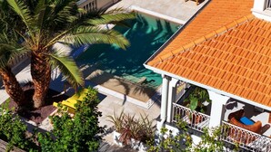 A rooftop pool area with a palm tree, yellow lounge chairs, and a white building with a tiled roof. - Luxury Authentic Italian Villa with Private Pool & Iconic Seaview Terrace (Massa Lubrense)