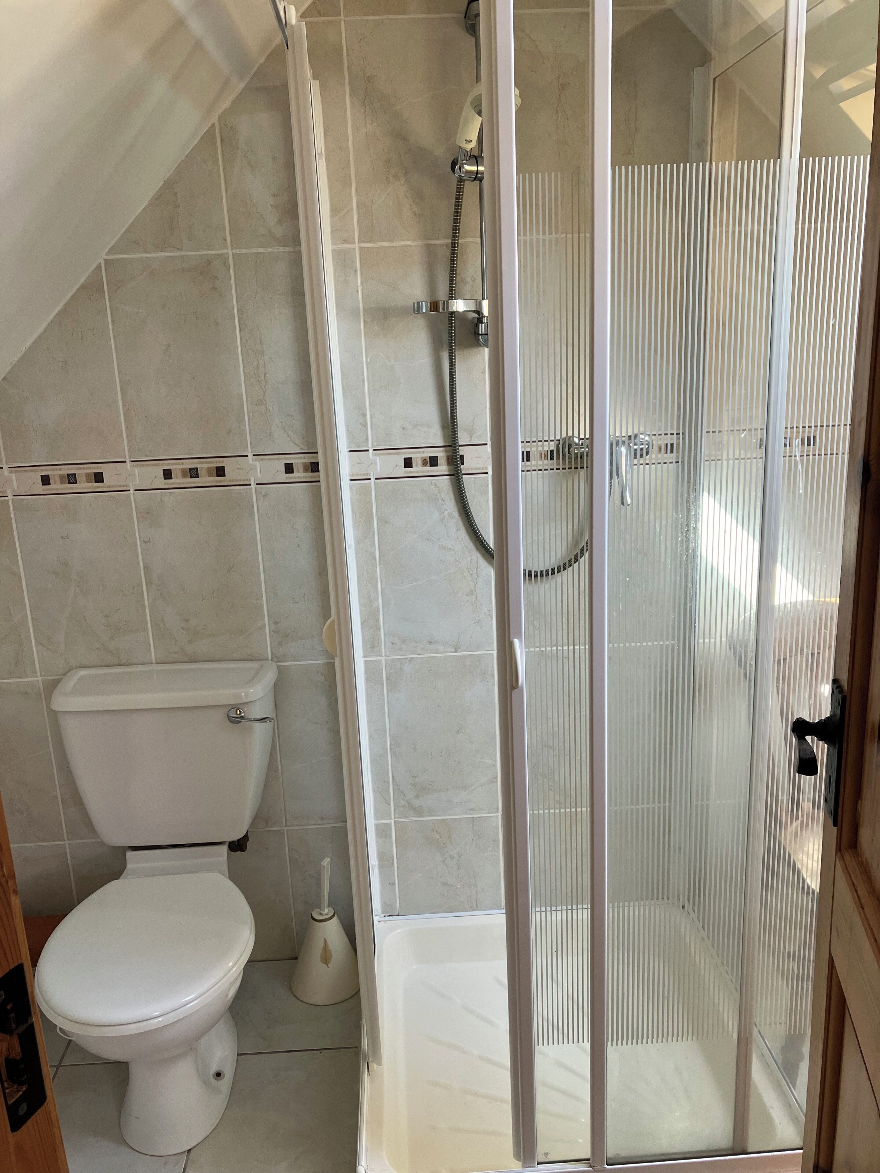 Une salle de bain avec des toilettes, une douche dotée d’une porte en verre et des murs carrelés.