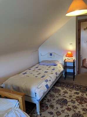 A single bed with a patterned bedspread, a bedside table with a lamp, and a patterned rug on the floor. - Cosy 200 year old 3 bedroom cottage in Clare 3 min drive to Doonbeg Golf Course (CE)