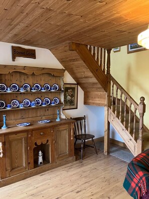 A wooden staircase with a wooden railing, a cabinet with blue and white plates, and a chair.